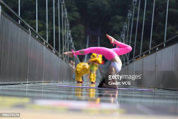 Girl performs yoga on a glass bridge featuring a circular observation deck along a cliff at the Gulongxia scenic spot on June 28, 2018 in Qingyuan,...