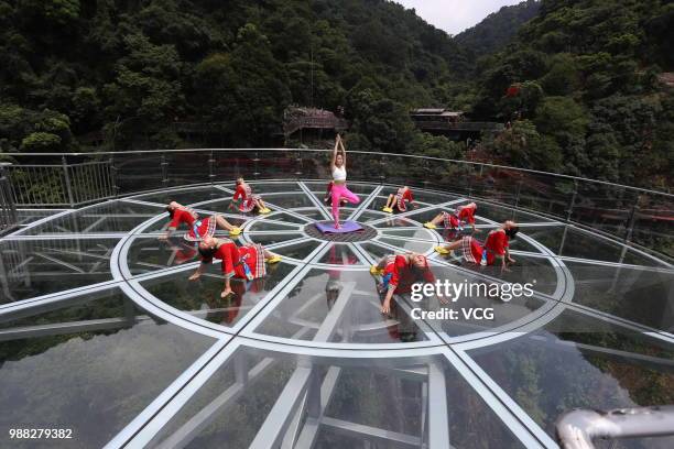 Girls perform yoga on a glass bridge featuring a circular observation deck along a cliff at the Gulongxia scenic spot on June 27, 2018 in Qingyuan,...