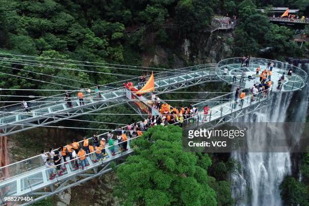Aerial view of tourists visiting a glass bridge featuring a circular observation deck along a cliff at the Gulongxia scenic spot on June 28, 2018 in...