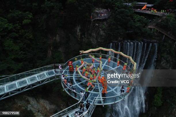 Aerial view of people performing dragon dance on a glass bridge featuring a circular observation deck along a cliff at the Gulongxia scenic spot on...
