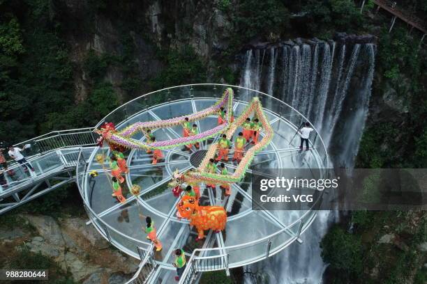 Aerial view of people performing dragon dance on a glass bridge featuring a circular observation deck along a cliff at the Gulongxia scenic spot on...