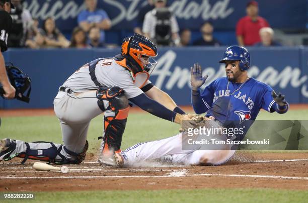 Devon Travis of the Toronto Blue Jays is tagged out at home plate while attempting to score as Grayson Greiner of the Detroit Tigers applies the tag...