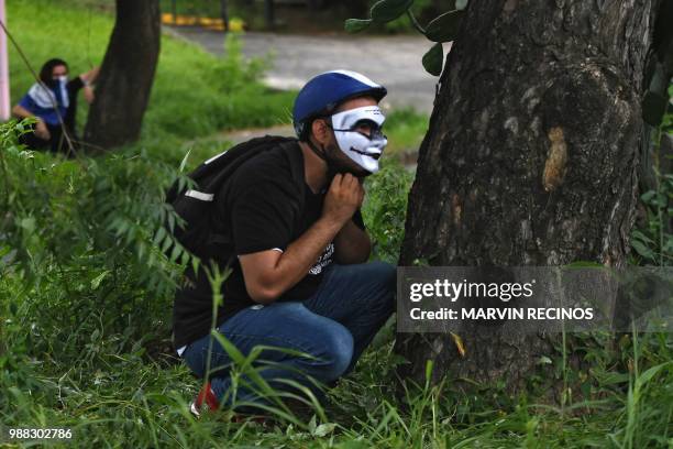 Anti-government protesters hide behind tress during clashes within the "Marcha de las Flores" in Managua, on June 30, 2018. - At least six people...