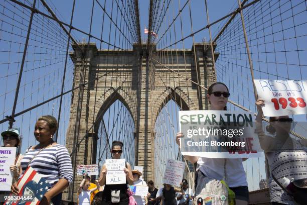 Demonstrators carry signs while marching across the Brooklyn Bridge during a protest against the Trump administration's policy on separating...