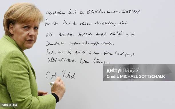 German Chancellor Angela Merkel writes a dedication on a wall as she visits the exhibition "Peaceful Revolution 1989/90" on May 4, 2010 at the...