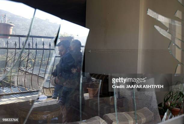 Relatives of Palestinian Islamic Jihad member Salah al-Bokhari are reflected on a shattered window following a raid by Israeli forces to arrest him...
