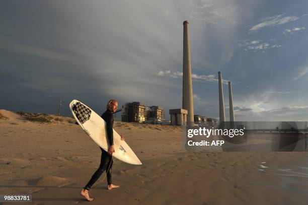 An Israeli surfer walks near chimneys of an electricity manufacturing station near the northern Israeli city of Hadera on December 7, 2009. World...