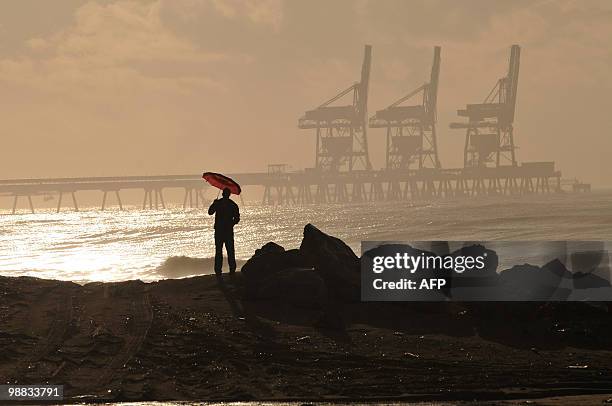 An Israeli man holds an umbrella as he stands opposite an electricity manufacturing station near the northern Israeli city of Hadera on December 7,...
