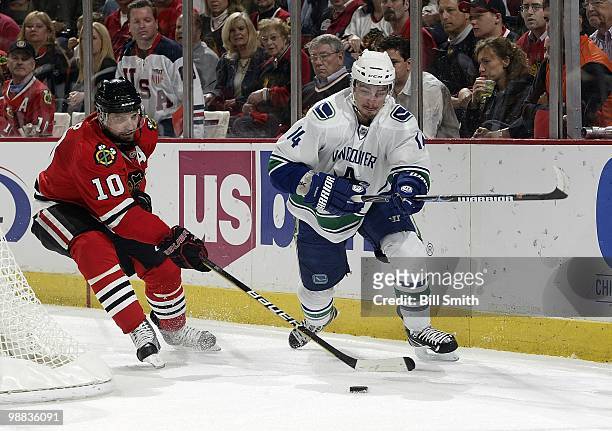 Patrick Sharp of the Chicago Blackhawks and Alexandre Burrows of the Vancouver Canucks chase the puck around the boards at Game One of the Western...
