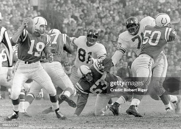 Johnny Unitas of the Baltimore Colts looks for a receiver as Art Spinney and Buzz Nutter block Andy Robustelli and Rosey Grier of the New York Giants...