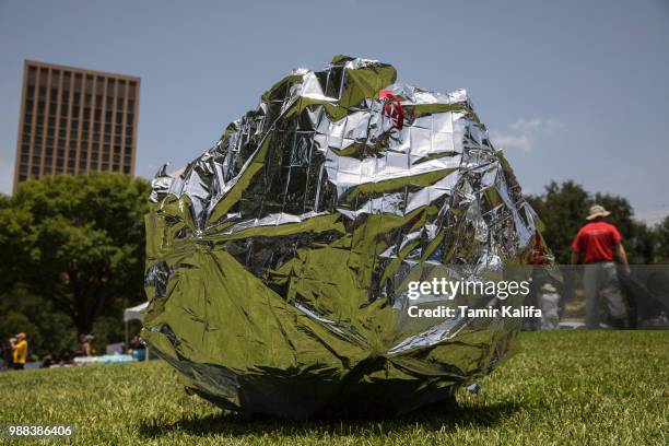 Children play with an umbrella wrapped in a space blanket, meant to represent the blankets provided at shelters for immigrant children, during a...