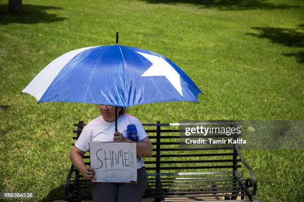 Henrietta Cameron-Mann holds a protest sign while sitting under an umbrella inspired by the Texas flag during rally against the Trump...