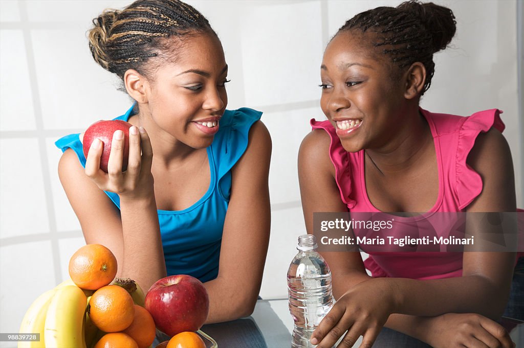Two teenage girls eating apple and drinking water