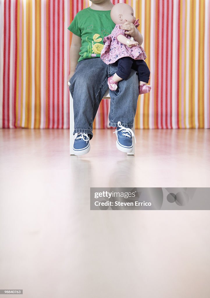 Young girl sitting in chair with doll on lap
