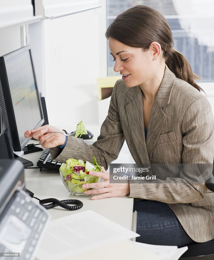 Young woman eating salad at office