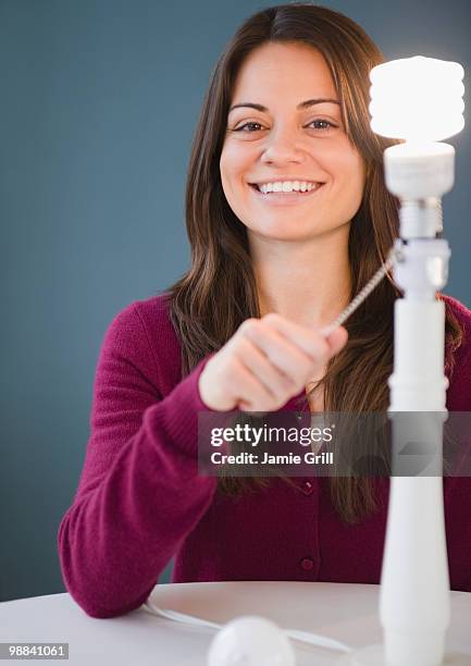 woman turning on energy saving lightbulb - bombilla de bajo consumo fotografías e imágenes de stock