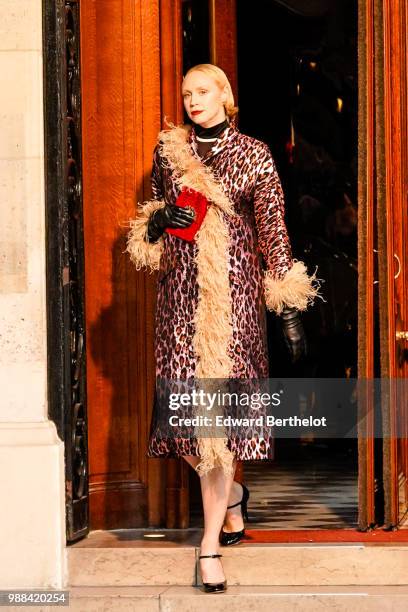 Gwendoline Christie wears a purple leopard print coat with brown fur, black shoes, holds a red clutch, during the Miu Miu Cruise Collection show,...