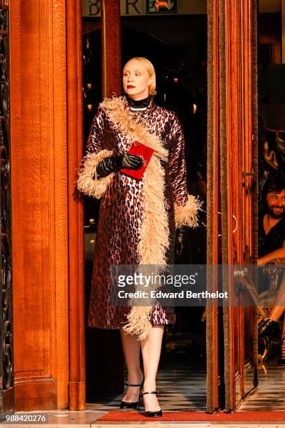 Gwendoline Christie wears a purple leopard print coat with brown fur, black shoes, holds a red clutch, during the Miu Miu Cruise Collection show,...