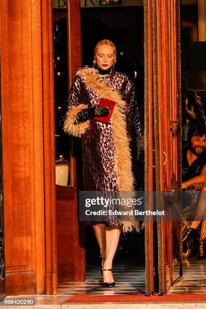 Gwendoline Christie wears a purple leopard print coat with brown fur, black shoes, holds a red clutch, during the Miu Miu Cruise Collection show,...