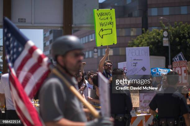 Protester decrying Trump administration immigration and refugee policies holds a sign pointing toward Pro-Trump counter demonstrators on June 30,...