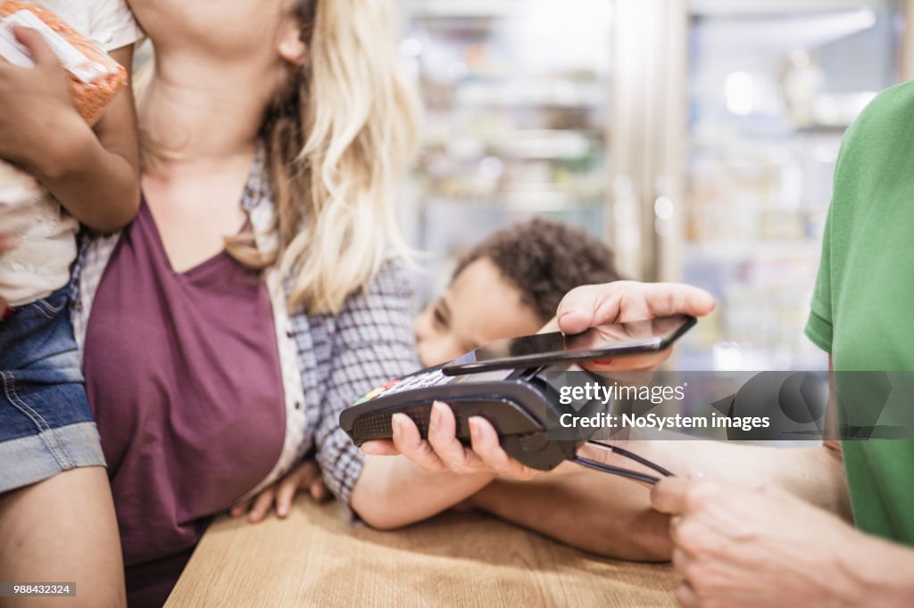 Single mother with her mixed-race kids is making a contactless payment at the store
