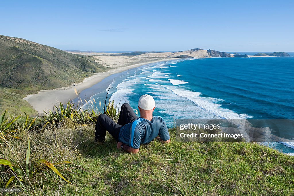 Northland, Cape Reigna, man laying on grass, looking towards beach