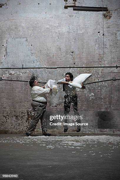 two men having pillow fight in warehouse - pillow fight stock pictures, royalty-free photos & images