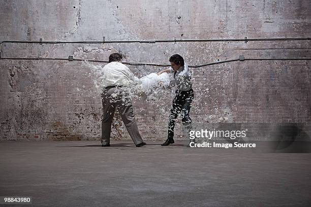 two men having pillow fight in warehouse - pillow fight stock pictures, royalty-free photos & images