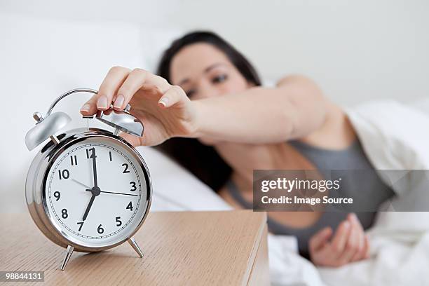 young woman reaching for alarm clock - alarmklok stockfoto's en -beelden