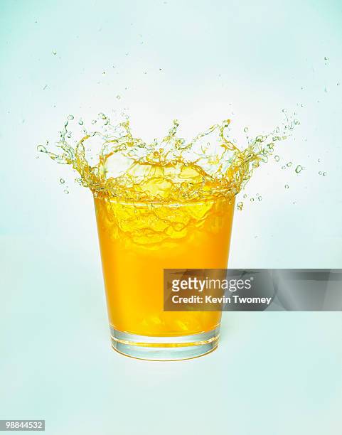 close up of orange juice splashing out of glass - orange juice stock-fotos und bilder