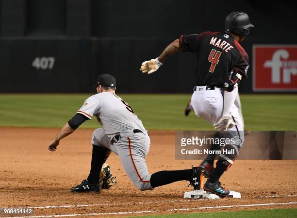 Ketel Marte of the Arizona Diamondbacks grabs the back of his right leg while crossing first base as Brandon Belt of the San Francisco Giants scoops...