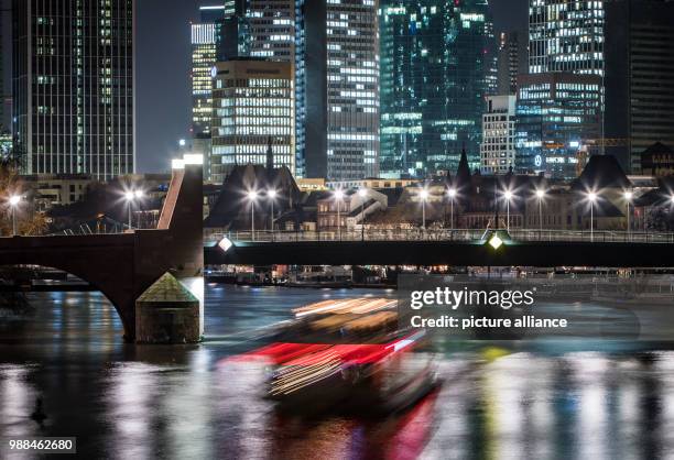 Pleasure barge drives under a bridge spanning the river Main, leaving a trail of light with 15 seconds of exposure time, in Frankfurt am Main,...