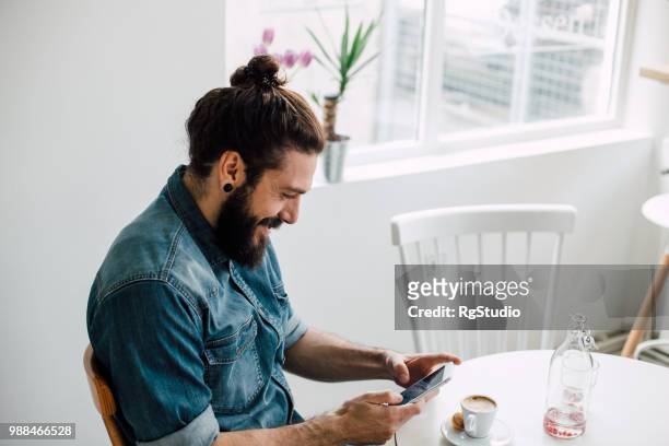 lachende jongeman te typen op zijn telefoon bij een winkel van de koffie - hair bun stockfoto's en -beelden