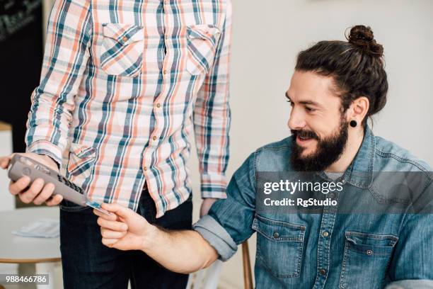 young man putting his credit card in a card reader - earring card stock pictures, royalty-free photos & images