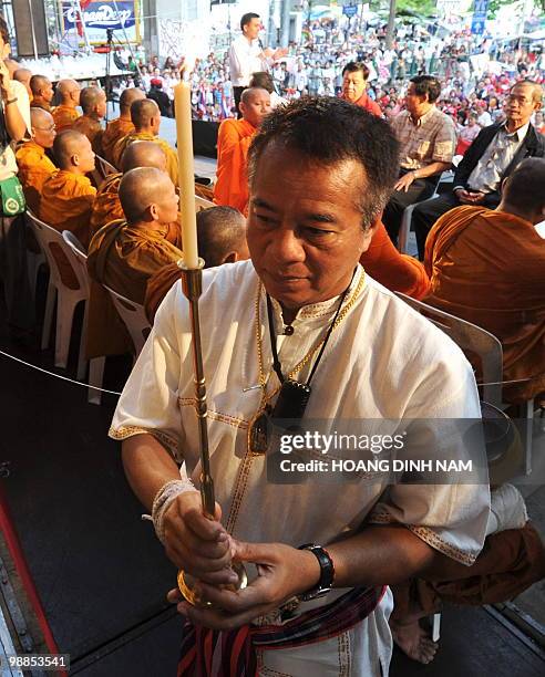 Thai "Red Shirt" anti-government protest leader Veera Musikapong holds a candle in front of a Buddha at the beginning of a ceremony, part of...