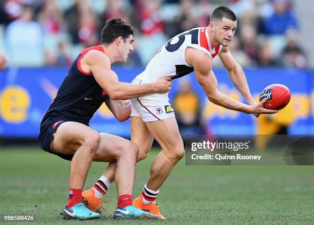 Jack Sinclair of the Saints handballs whilst being tackled by Christian Petracca of the Demons during the round 15 AFL match between the Melbourne...