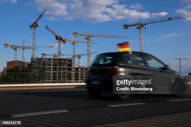 Construction cranes stand above the Europacity project residential building site as a German national flag flies from a passing automobile in Berlin,...