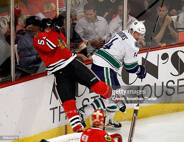 Alexandre Burrows of the Vancouver Canucks checks Brian Campbell of the Chicago Blackhawks into the boards behind the net as Antti Niemi watches in...