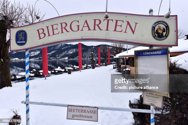 Sign reads "Biergarten" and "Seeterrasse geschlossen" at the snow-covered garden area on the banks of Schliersee lake in Schliersee, Germany,...