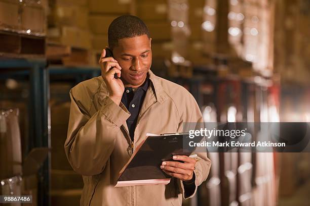 black man working in warehouse and talking on cell phone - mark atkinson stock pictures, royalty-free photos & images