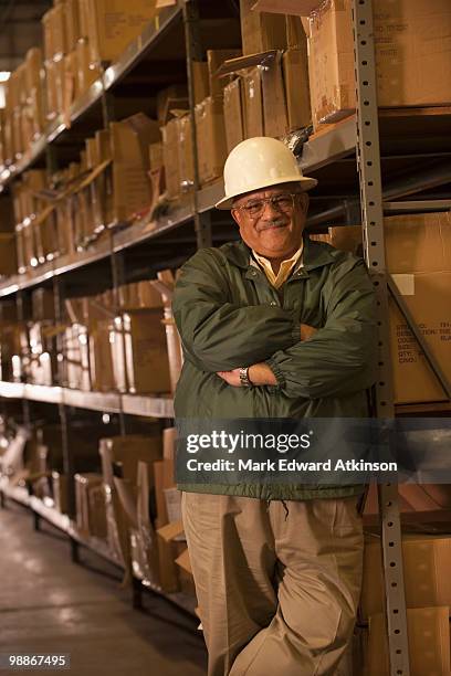 mixed race man in hard-hat in warehouse - mark atkinson stock pictures, royalty-free photos & images