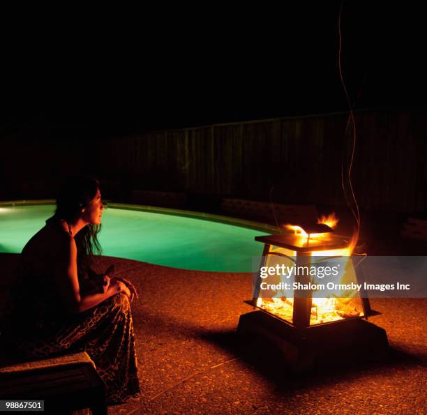 hispanic woman sitting near fire pit near swimming pool - hot latin nights stock pictures, royalty-free photos & images