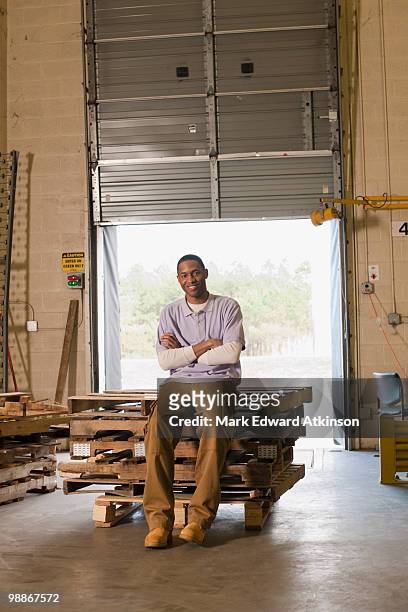 black man sitting on pallets in warehouse - mark atkinson stock pictures, royalty-free photos & images