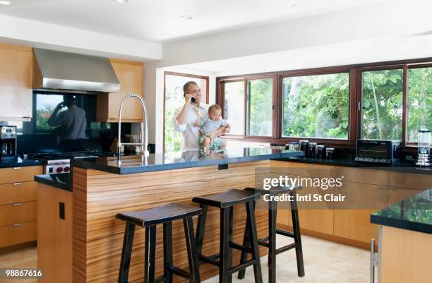 father holding son and talking on phone in kitchen - inti st clair stock pictures, royalty-free photos & images