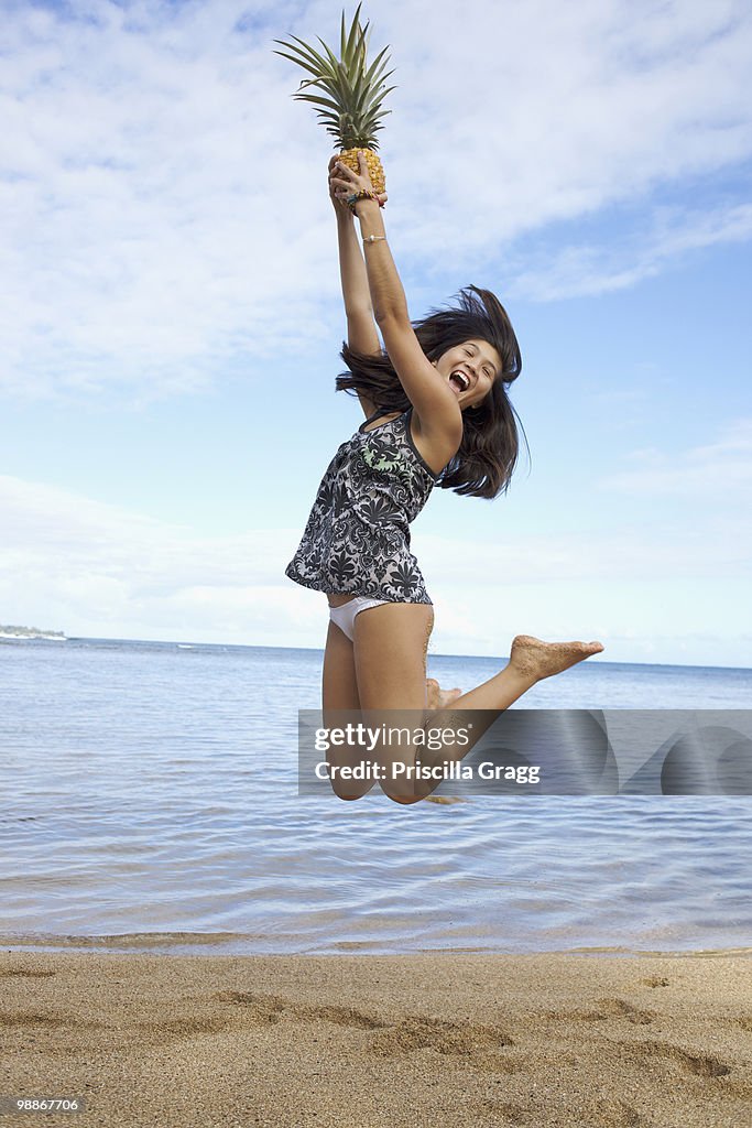 Mixed race teenager jumping and holding pineapple on beach
