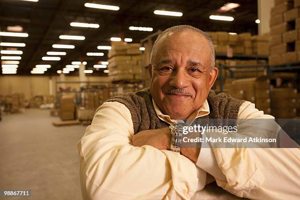 mixed race man with arms crossed in warehouse - mark atkinson stock pictures, royalty-free photos & images