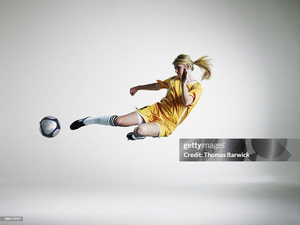 Female soccer player kicking ball in mid air 