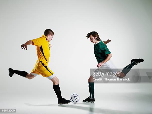 two male soccer players converging on ball - confrontación fotografías e imágenes de stock