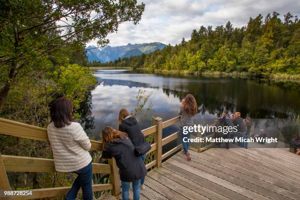 hikers explore the lake matheson trails. the lakes mirror reflections are a famous photo stop for visitors. - serra cook - fotografias e filmes do acervo