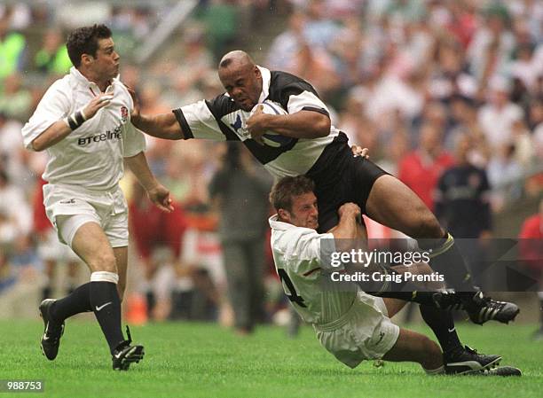 Jonah Lomu of the Barbarians is tackled by Paul Sampson of England, with Martyn Wood closing in during the match between England and the Barbarians...